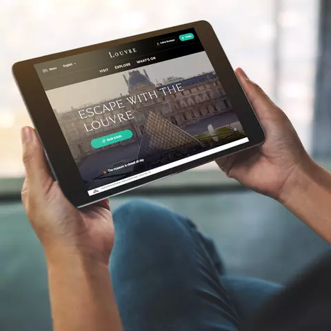 Aufsicht auf ein Tablet mit der Website des Louvre, dass eine junge Frau in den Händen hält
